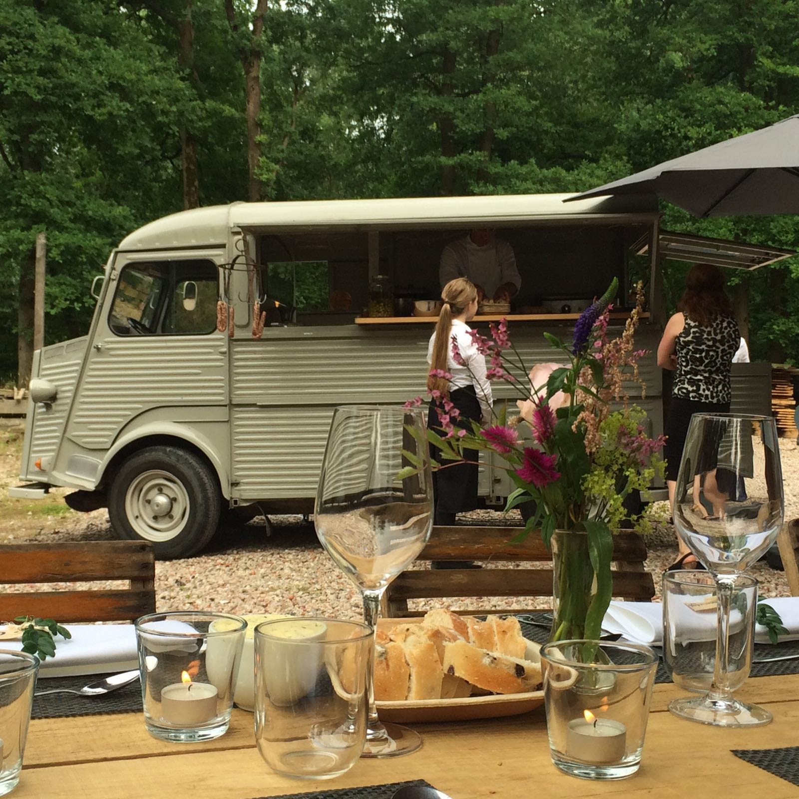 De Citroën HY met open luik in het bos, op de voorgrond een gedekte tafel met brood, kaarsjes en bloemen