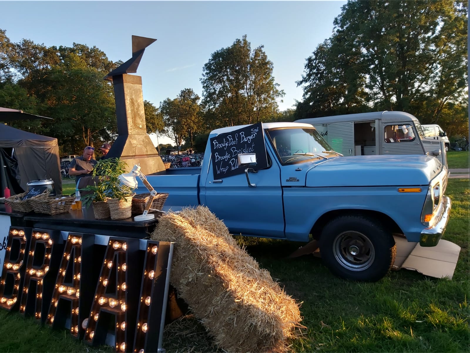 De blauwe Ford F150 met de braai en lichtletters BRAAI in het gras, bij laag zonlicht
